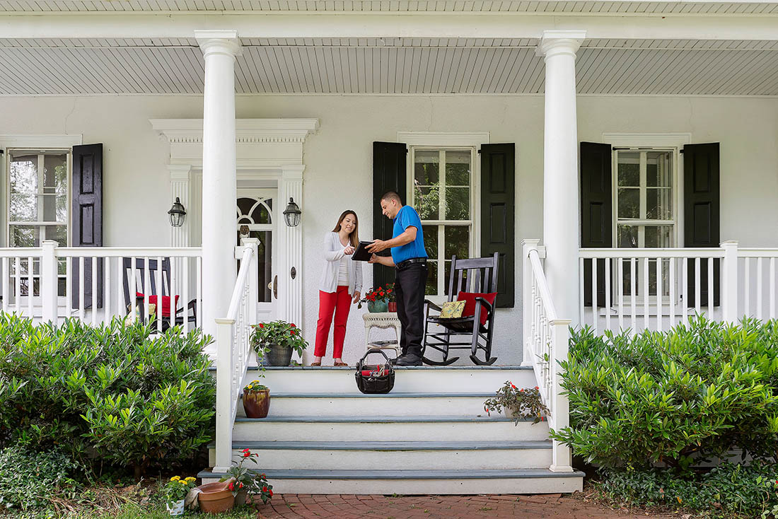 Homeowner standing on front porch discussing HVAC service with a technician