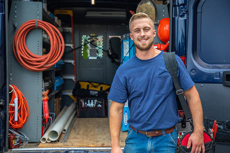 HVAC technician smiling standing next to service vehicle filled with tools
